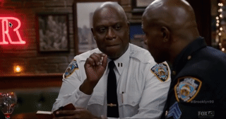 Captain Holt from Brooklyn Nine-Nine grimacing while lighting a cigar in a dimly lit bar